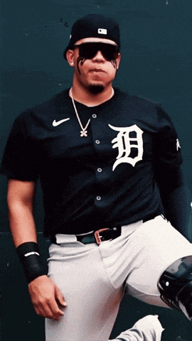 a man wearing a tigers jersey stands in front of a green wall