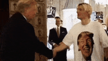 a man wearing a donald trump shirt is shaking hands with a man in a suit .