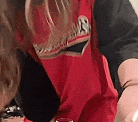 a person wearing a red shirt with a skull on it is drinking from a glass .