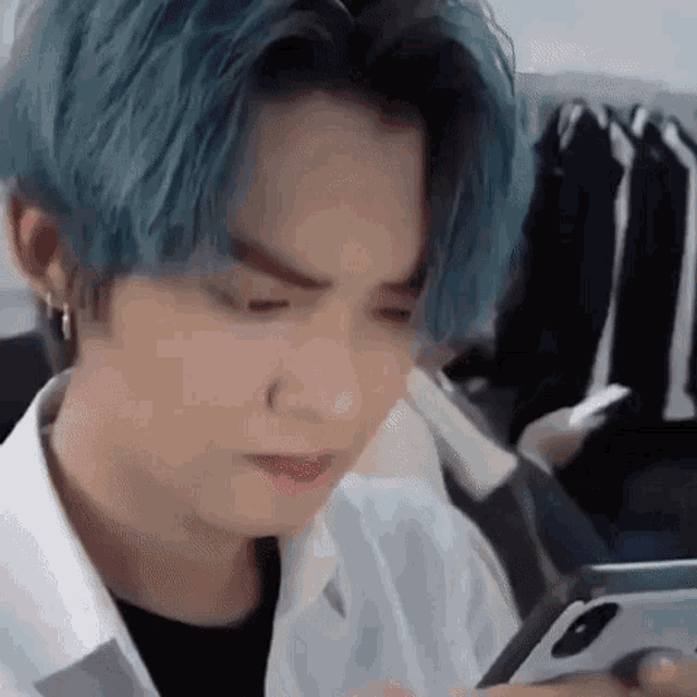 a young man with blue hair is looking at his phone .