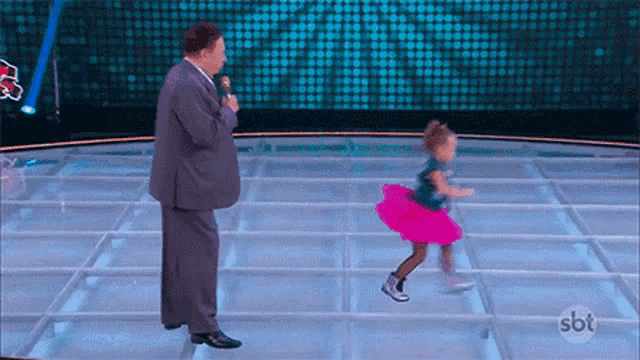 a little girl in a pink tutu is dancing with a man in a suit on a stage .