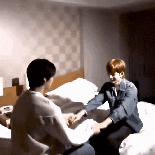 two young men are sitting on a bed and holding hands