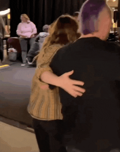 a woman with purple hair is hugging a man with black hair