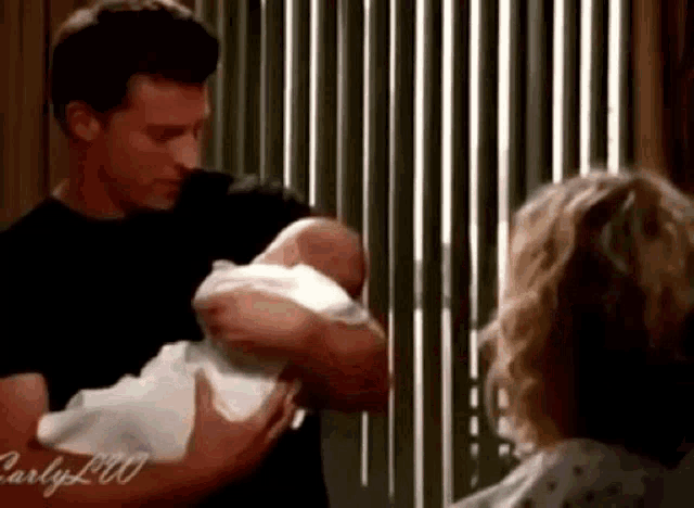 a man is holding a baby in his arms next to a woman in a hospital gown .