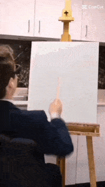 a man in a suit is sitting at an easel pointing at a white board .