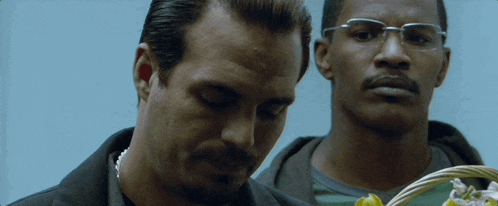 two men are standing next to each other and one of them is wearing glasses