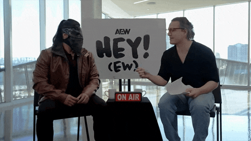 two men are sitting in front of a sign that says aew hey