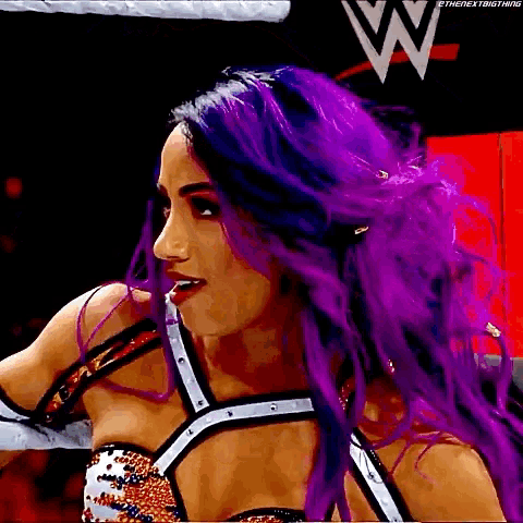 a woman with purple hair is standing in a wrestling ring and looking at the camera .