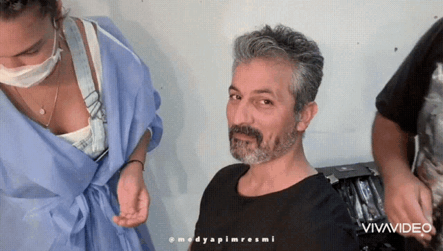 a man with a beard is getting his hair done by a woman with a mask on