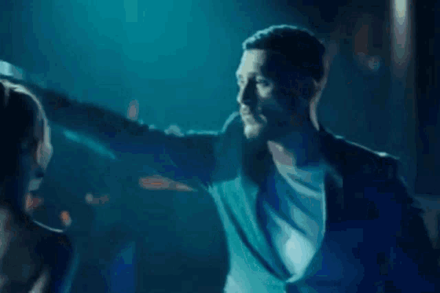 a man in a blue suit is talking to another man in a dark room .