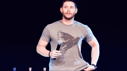 a man is standing on a stage with a microphone in his hand and his shirt is open .