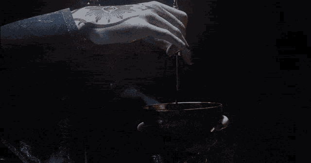 a person with a tattoo on their hand pours something into a cup