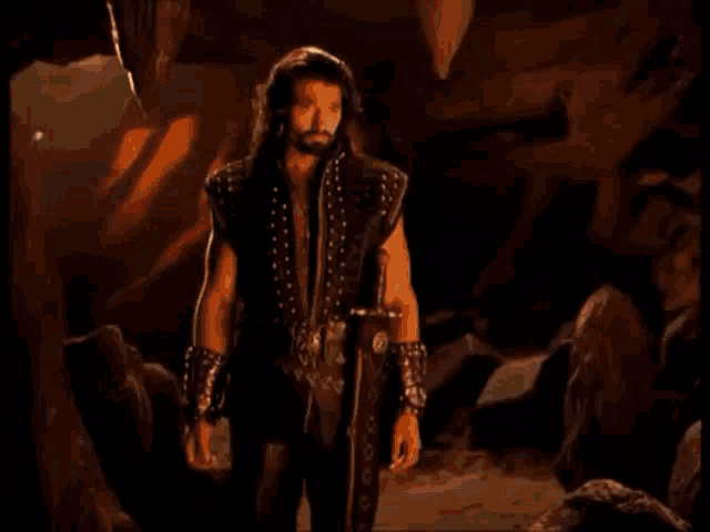 a man is standing in the middle of a cave surrounded by rocks and fire .