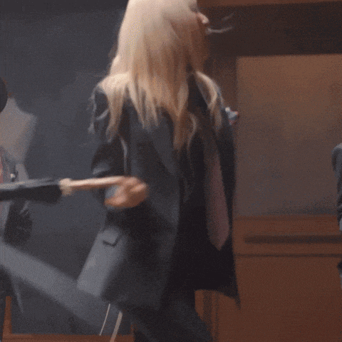 a woman in a suit and tie is dancing with a smiley face in the background