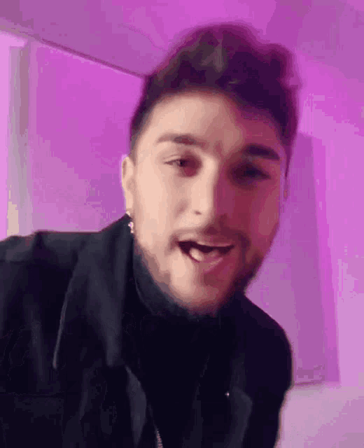 a man with a beard is wearing a black jacket and earrings and is making a funny face .