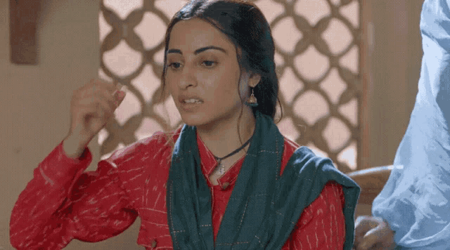 a woman wearing a red shirt and a blue scarf looks angry