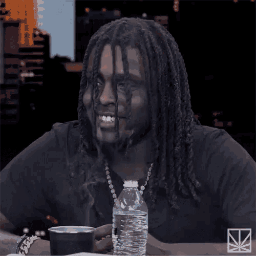 a man with dreadlocks sits at a table with a bottle of water and a cup