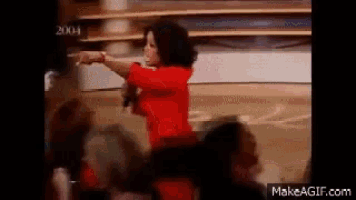 a woman in a red dress is pointing at something in front of a crowd of people .