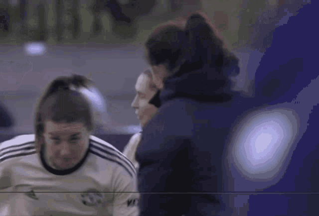 a woman in a white adidas shirt is talking to another woman in a blue jacket .