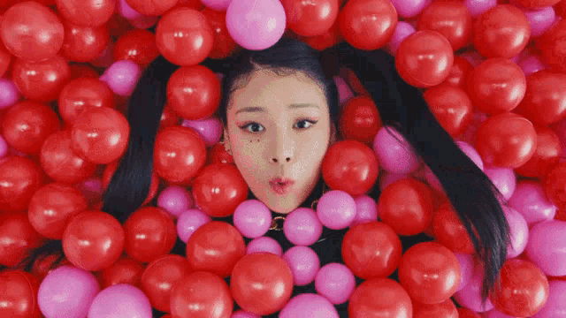 a girl is surrounded by red and pink balloons