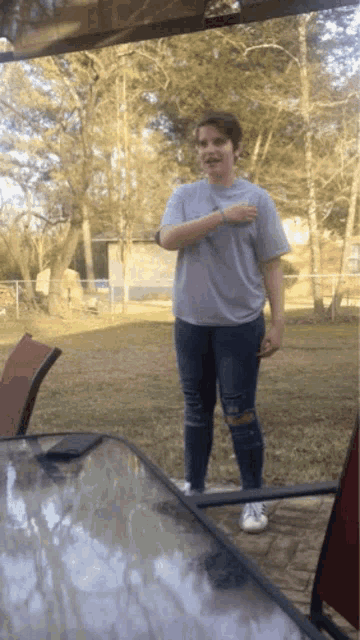 a girl in a gray shirt and ripped jeans is standing in front of a table