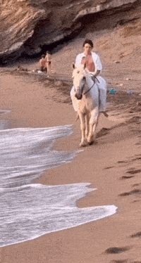 a man riding a white horse on a sandy beach