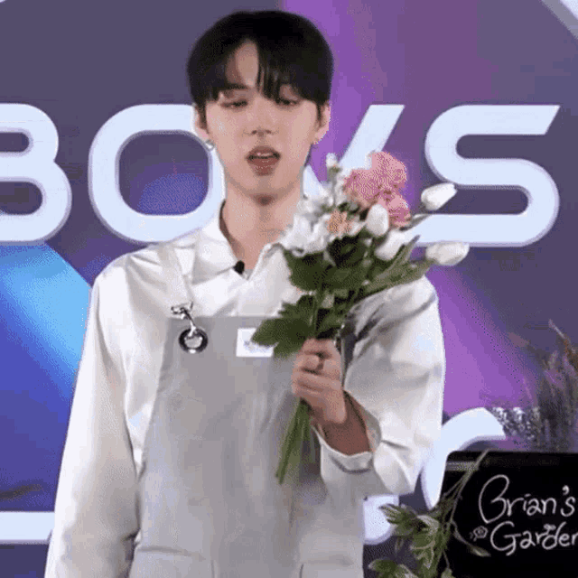 a man in an apron holds a bouquet of flowers in front of a sign that says brian 's garden