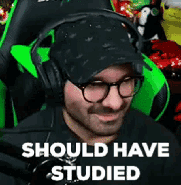 a man wearing glasses and headphones is sitting in a green chair with the words `` should have studied '' above him .