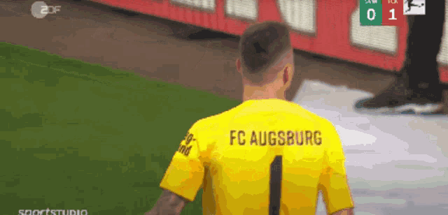 a soccer player wearing a yellow shirt with the word augsburg on the back