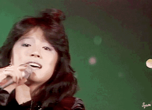 a close up of a woman singing into a microphone with the word syria on the bottom right