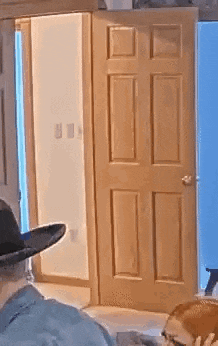 a man wearing a cowboy hat is standing in front of a wooden door .