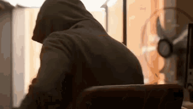 a man in a hooded jacket is sitting at a desk with a laptop .