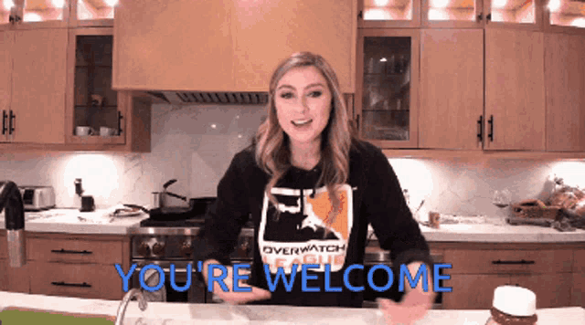 a woman standing in a kitchen wearing an overwatch league shirt