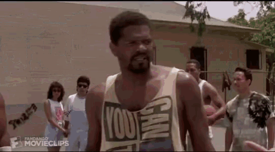 a man wearing a yellow tank top with the words `` you can '' on it is standing in front of a group of people .