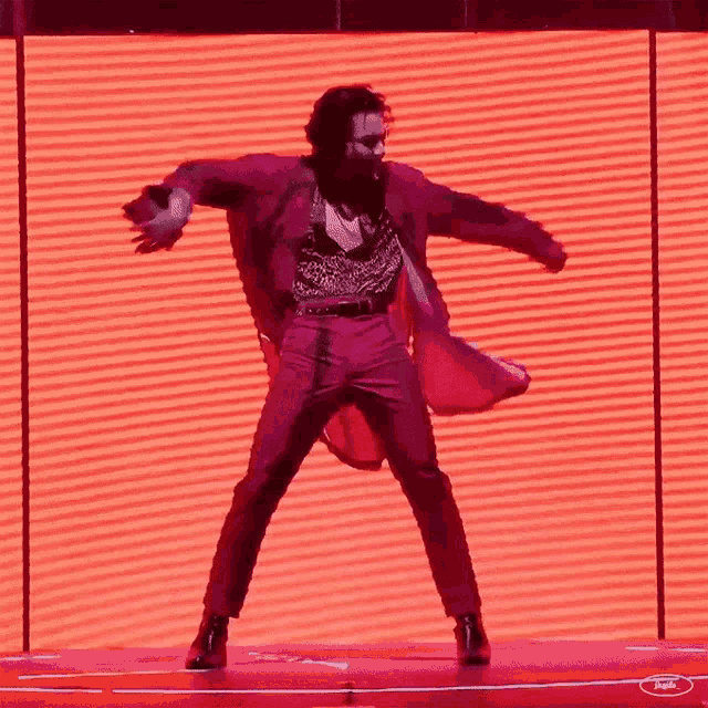 a man in a red suit is dancing on a stage in front of a red screen .
