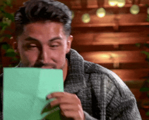 a man in a sweater is holding a piece of green paper
