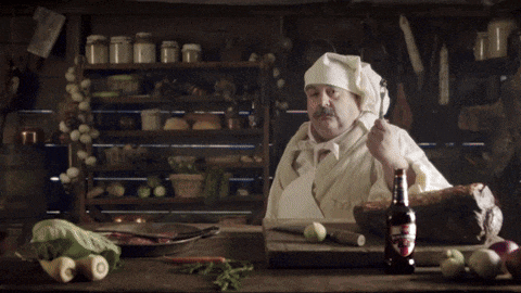 a man in a chef 's hat is standing in front of a table with a bottle of beer