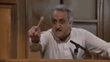 a man is giving a speech in front of a microphone in a courtroom and pointing at the camera .