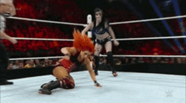 two women are wrestling in a ring with a referee watching