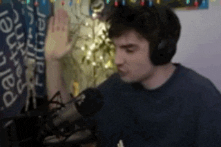 a man wearing headphones is sitting in front of a microphone and giving a high five .