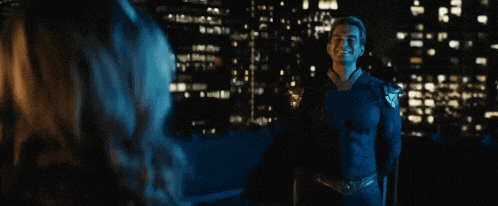 a man in a superhero costume is smiling at a woman in front of a city skyline at night