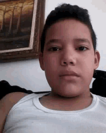 a young boy in a white tank top is making a funny face in front of a painting .