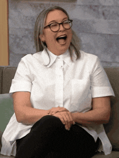 a woman wearing glasses is laughing while sitting on a couch