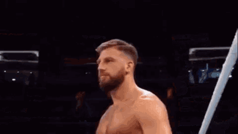a shirtless man with a beard is standing in a wrestling ring .