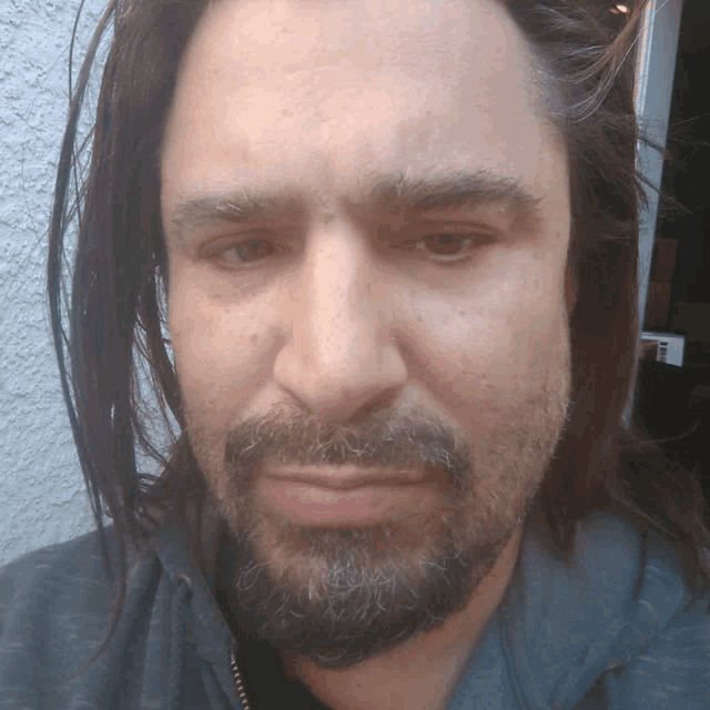 a man with long hair and a beard looks at the camera with a serious look on his face