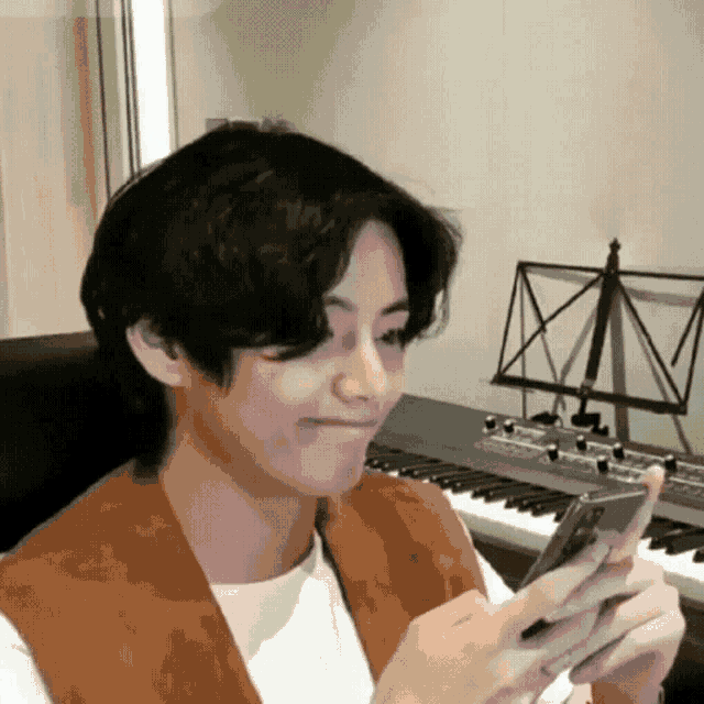 a young man is sitting at a piano holding a cell phone .