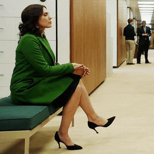 a woman in a green coat is sitting on a bench in a hallway