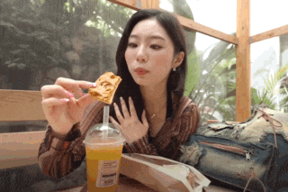 a woman is sitting at a table with a cup of orange juice and a piece of food in her hand
