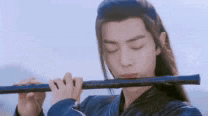 a young man with long hair is playing a flute .