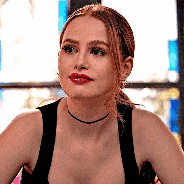 a woman wearing a choker and red lipstick is sitting at a table .